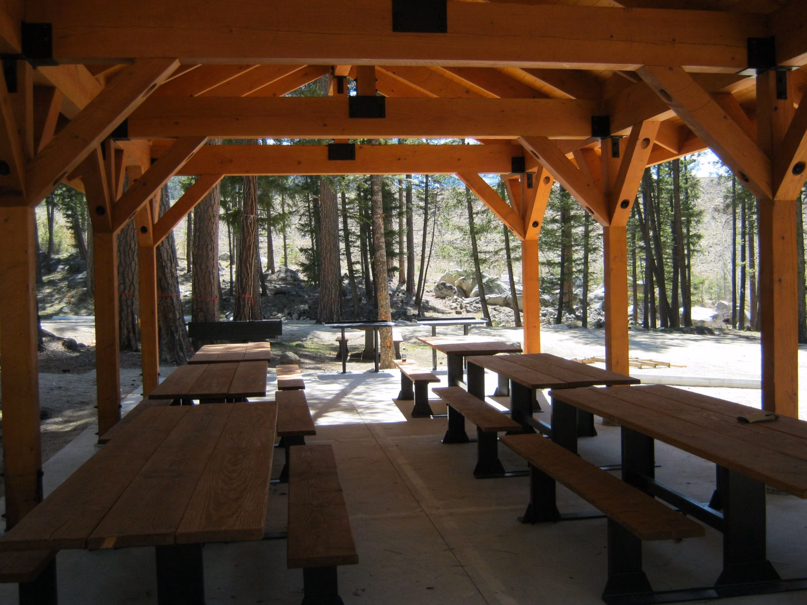 Rows of picnic tables under a timber-frame shelter in the woods