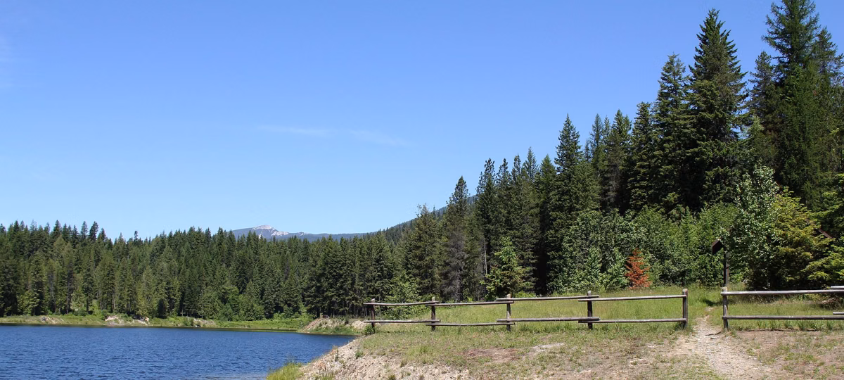 A day-use area with a split-rail fence beside a calm lake lined with firs