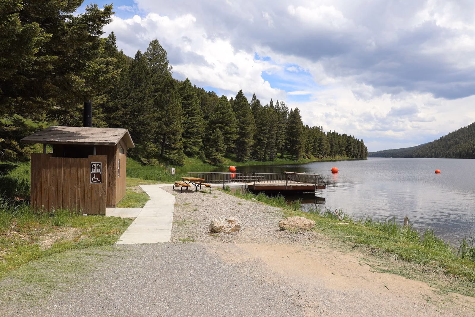 A short fishing pier and picnic area on a lake bordered by conifers