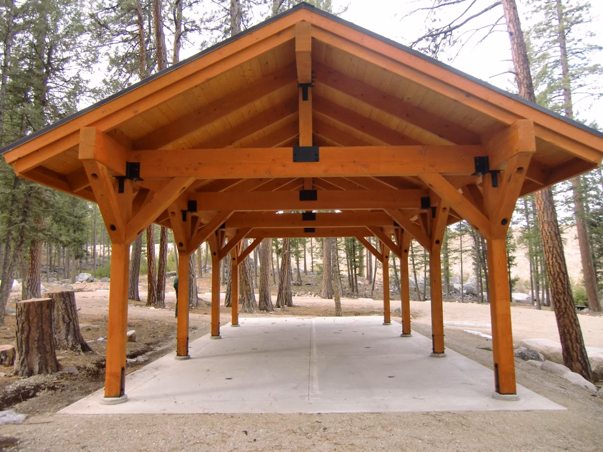 A timber-frame picnic shelter with tables in a pine forest